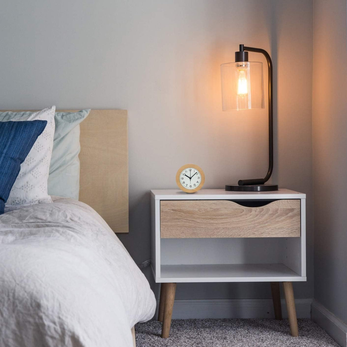 Wooden alarm clock on a white nightstand beside a glowing lamp