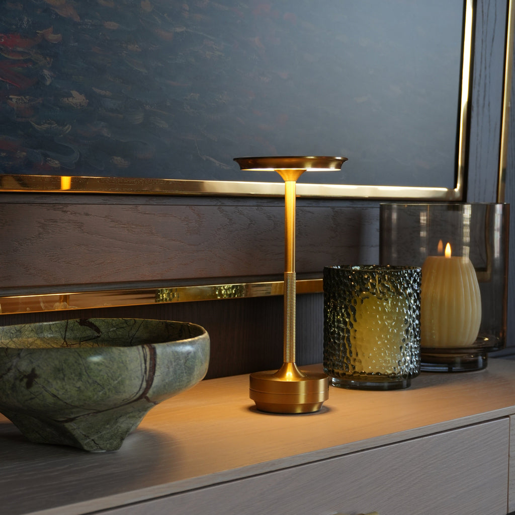 Gold table lamp on a sideboard beside candles and stone bowl