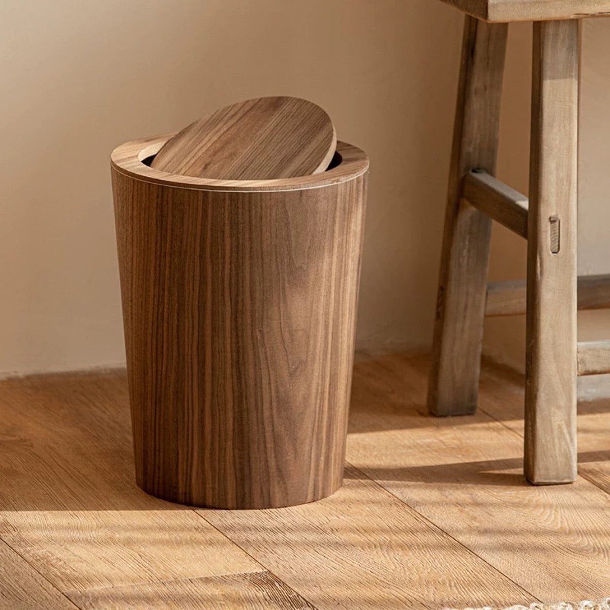 Walnut wood grain trash can next to a rustic wooden stool