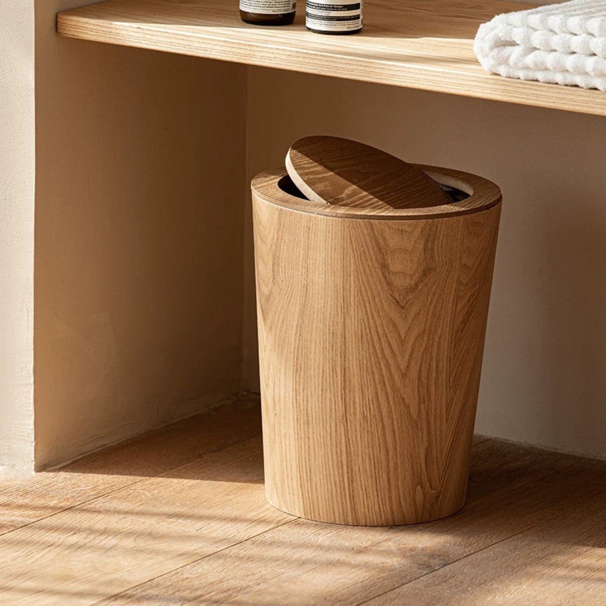 Natural trash can under a bathroom shelf with folded towels