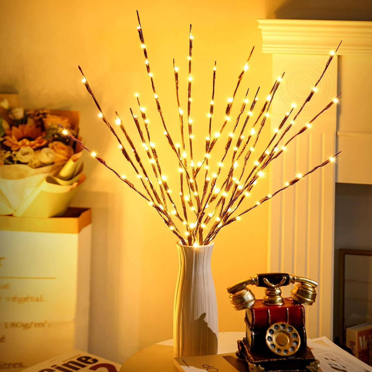 Faux lighted twigs in a white vase beside a vintage phone