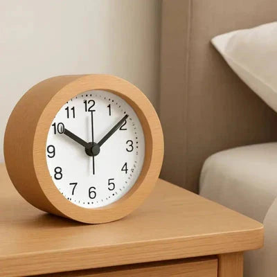 Round wooden alarm clock with white dial on a bedside table