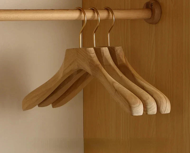 Three wide shoulder wooden hangers on a closet rail