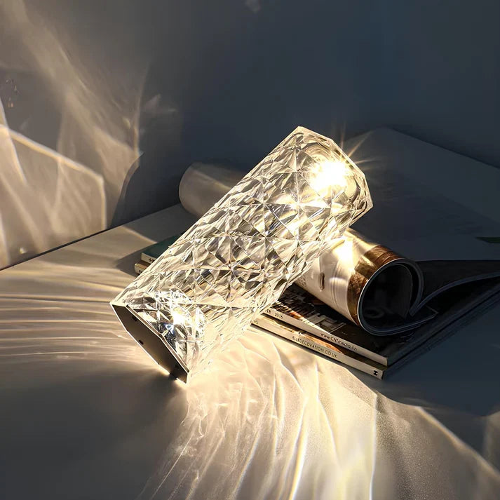 Faceted acrylic lamp lying on magazines, scattering warm light
