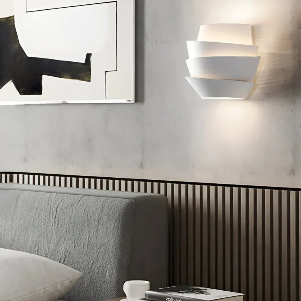 White wall sconce above a gray bed beside abstract art