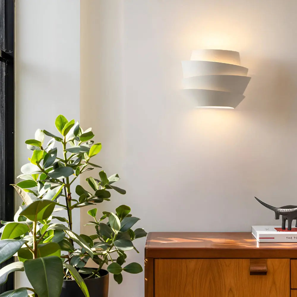Modern wall sconce glowing above a wooden dresser and plant