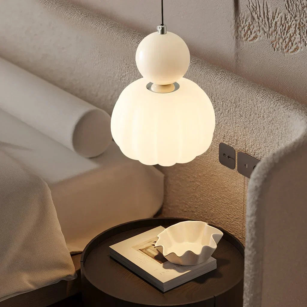 Cream hanging ceiling lamp glowing above a round bedside table
