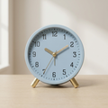 Dusty blue silent table clock on a light wood surface