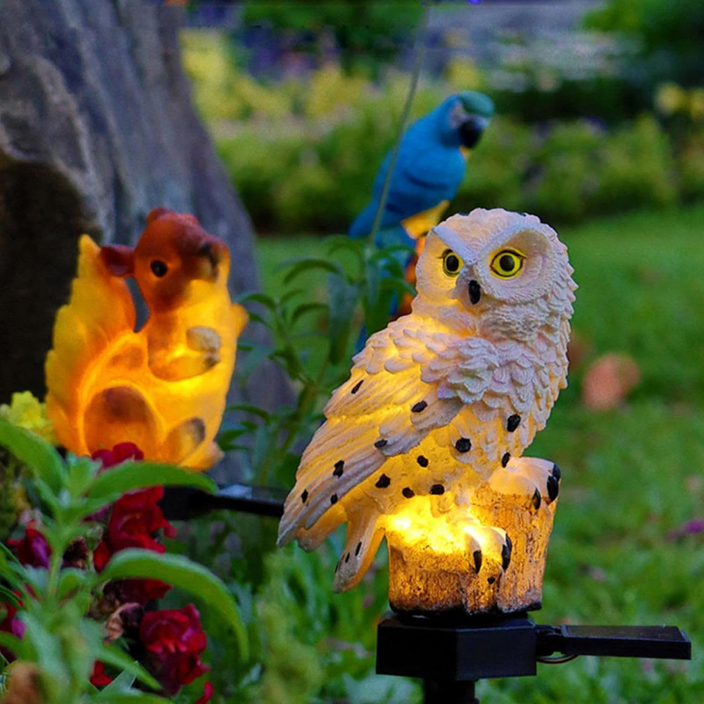 Solar owl stake light among garden flowers at evening