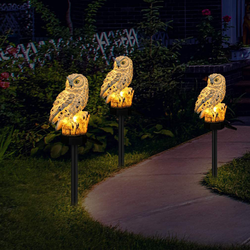 Three owl lights lining a garden path at night