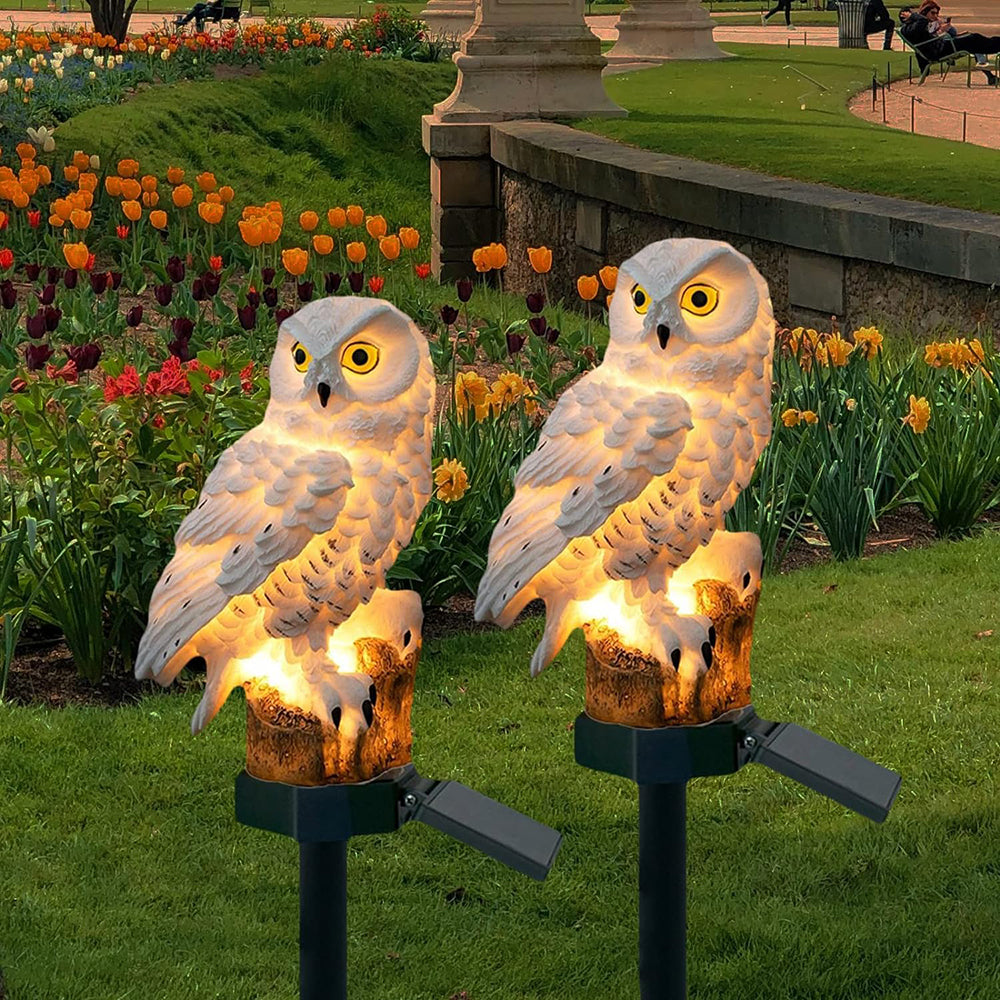 Two solar owl stake lights glowing in a tulip garden
