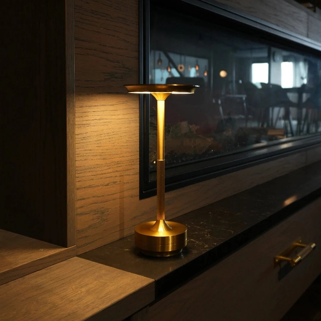 Gold cordless table lamp glowing on a dark stone ledge