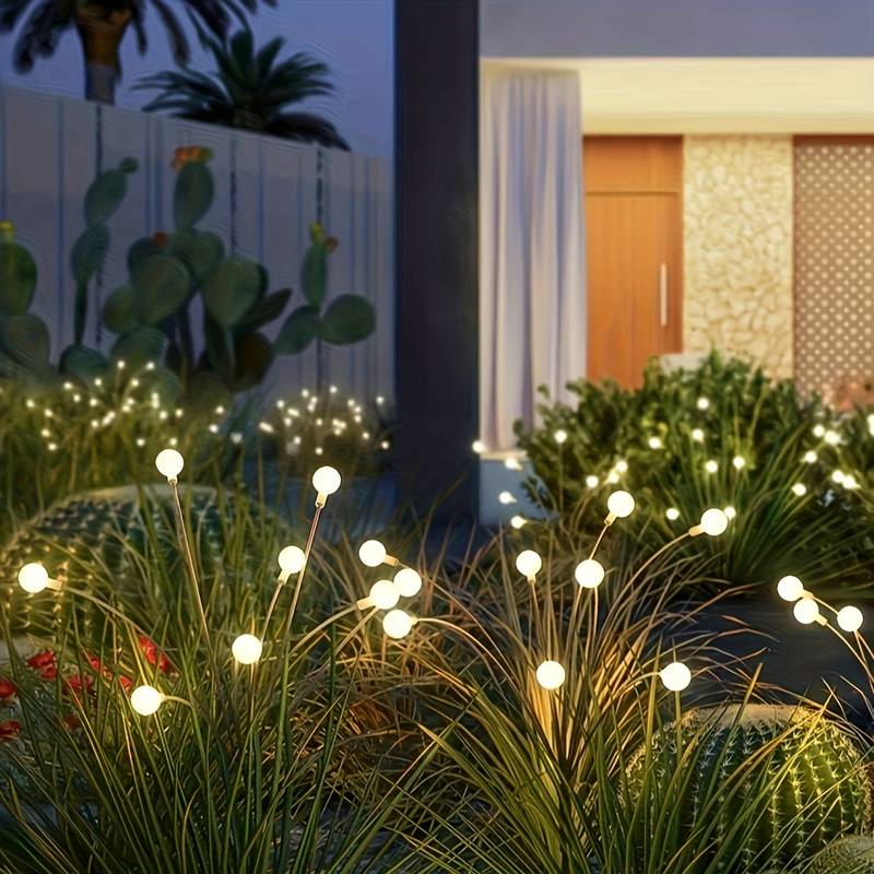 Solar stake lights glowing among grasses and cacti near a home