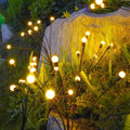 Solar garden stakes glowing among ferns beside a rock