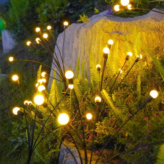 Solar garden stakes glowing among ferns beside a rock